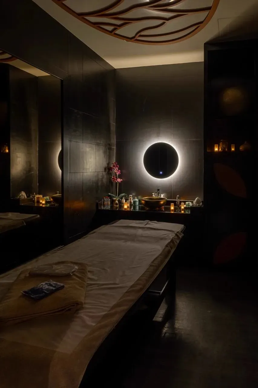 Dark treatment room with two round backlit mirrors and a massage table